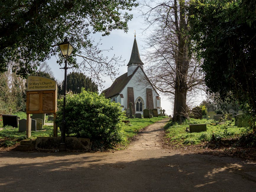 A peaceful garden pathway leading towards St. Mary's Church and Memorial Hall, with a white-painted Gothic Revival-style church featuring pointed arched windows and a tall, dark spire in the backgroun